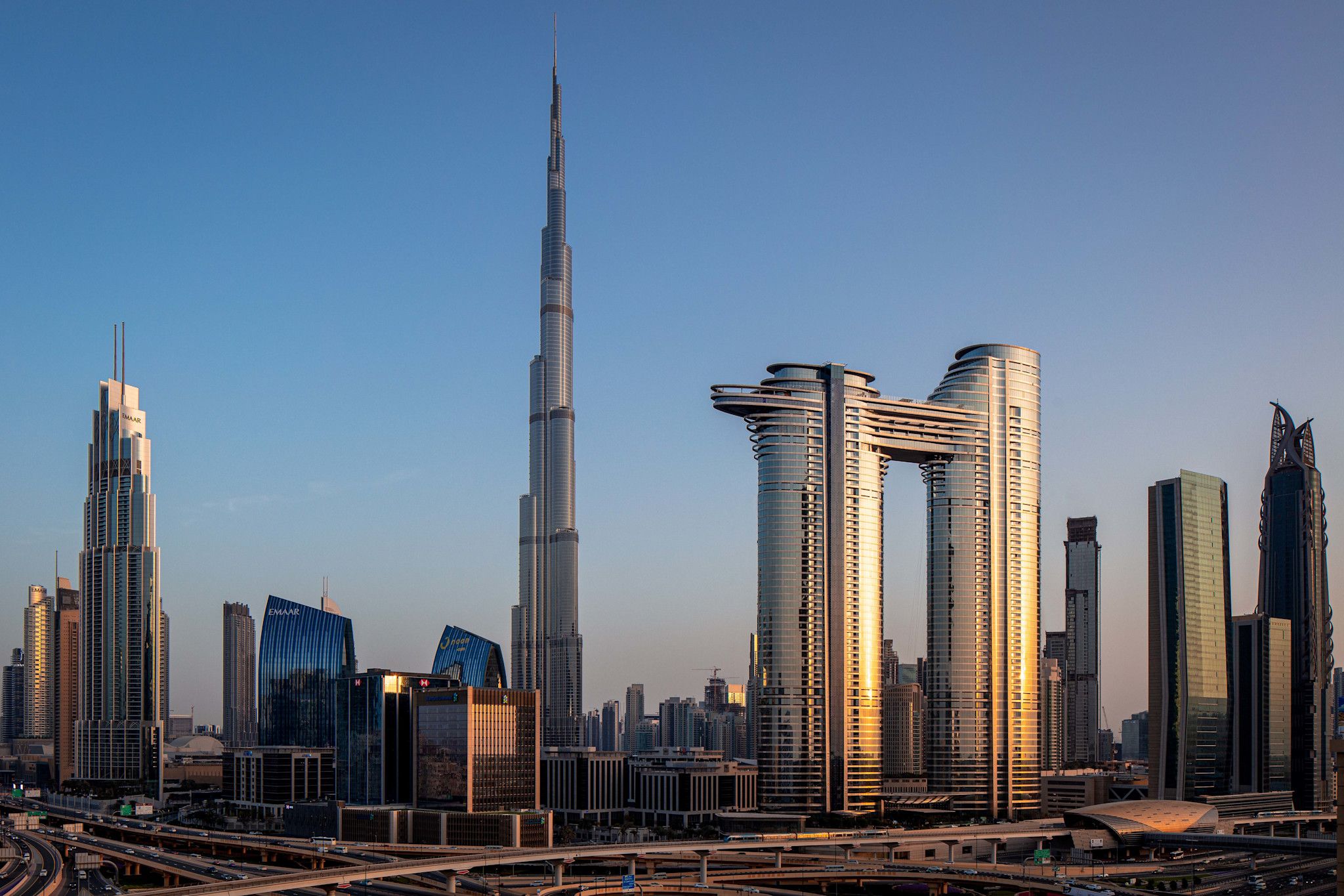 Address Sky View in Downtown Dubai at golden hour, its twin towers and the suspended sky bridge connecting them standing against the skyline beside the Burj Khalifa.