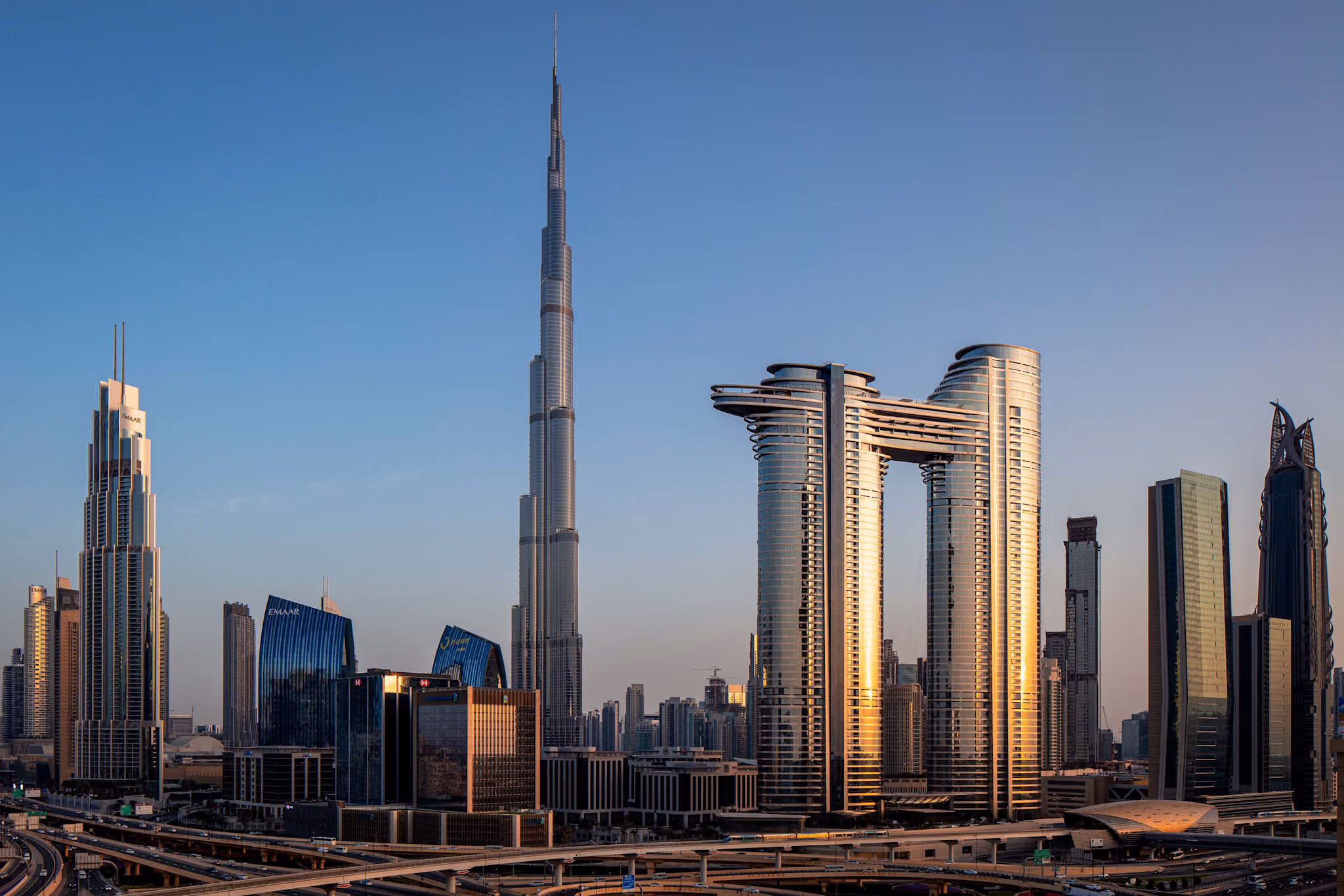 Address Sky View in Downtown Dubai at golden hour, its twin towers and the suspended sky bridge connecting them standing against the skyline beside the Burj Khalifa.