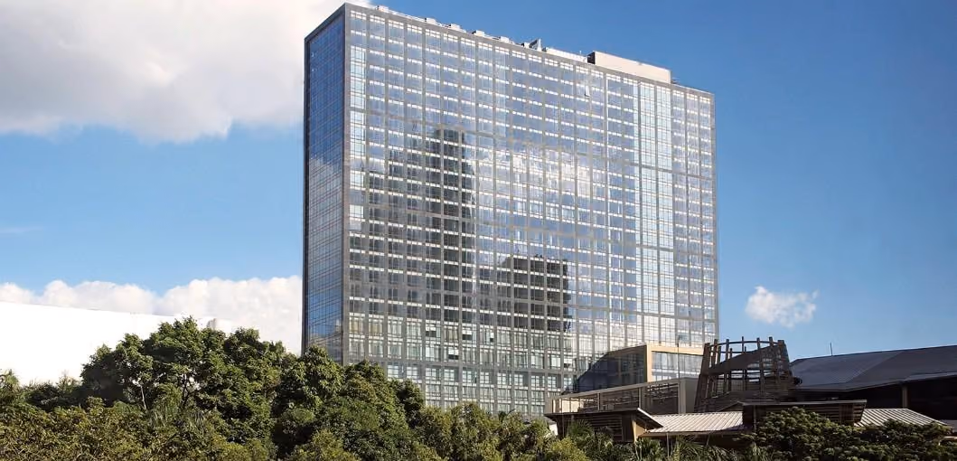 The glazed tower of Fairmont & Raffles Makati rising above the tree line in Manila, under a bright sky.