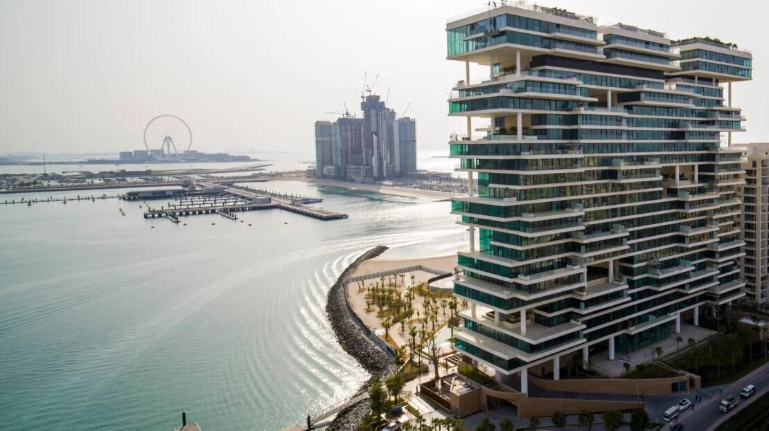 One Palm by Dorchester Collection on Palm Jumeirah, its stacked terraces glazed from floor to ceiling, seen across the water towards Bluewaters and Ain Dubai.