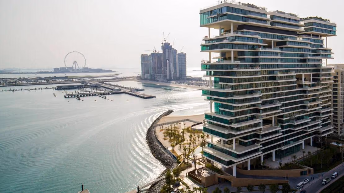 One Palm by Dorchester Collection on Palm Jumeirah, its stacked terraces glazed from floor to ceiling, seen across the water towards Bluewaters and Ain Dubai.