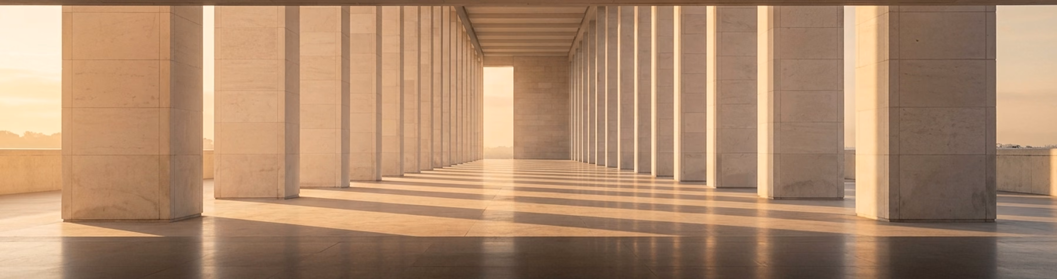 A limestone colonnade at sunrise, long shafts of low light falling across the polished stone floor between the piers.