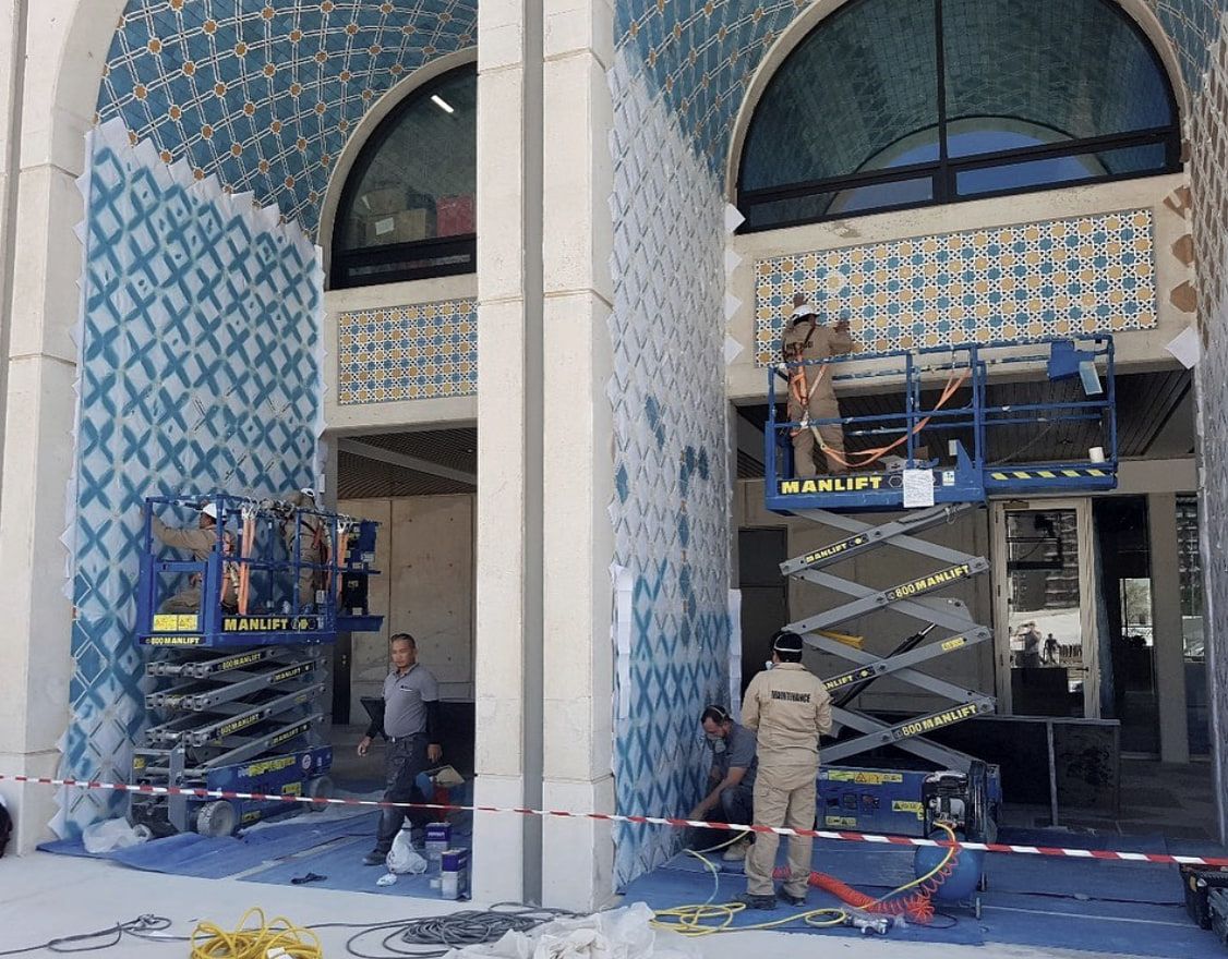 The Solution’s technicians on manlifts restoring the patterned ceramic tilework of Qasr Al Hosn, with protective sheeting over the surrounding surfaces.