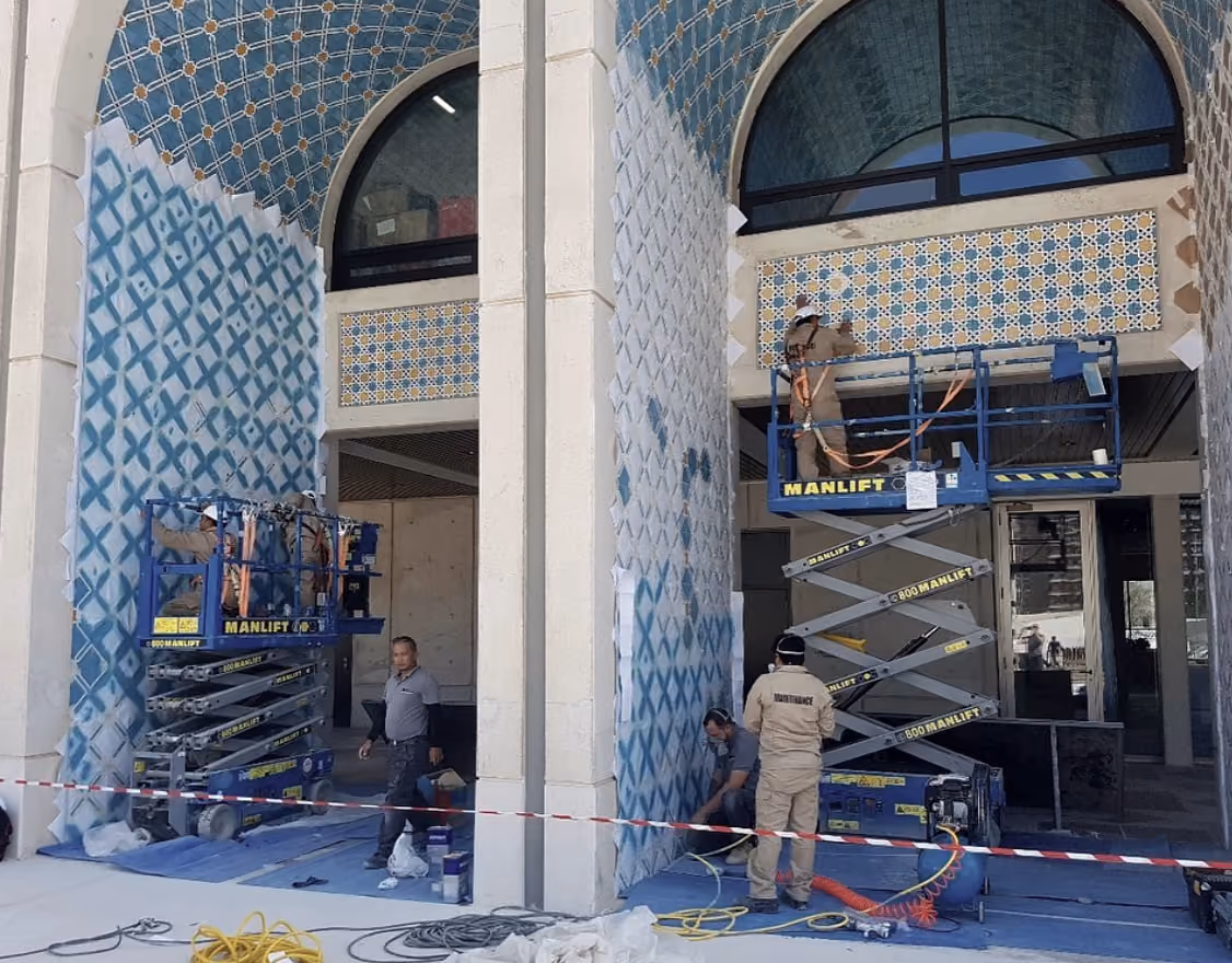 The Solution’s technicians on manlifts restoring the patterned ceramic tilework of Qasr Al Hosn, with protective sheeting over the surrounding surfaces.