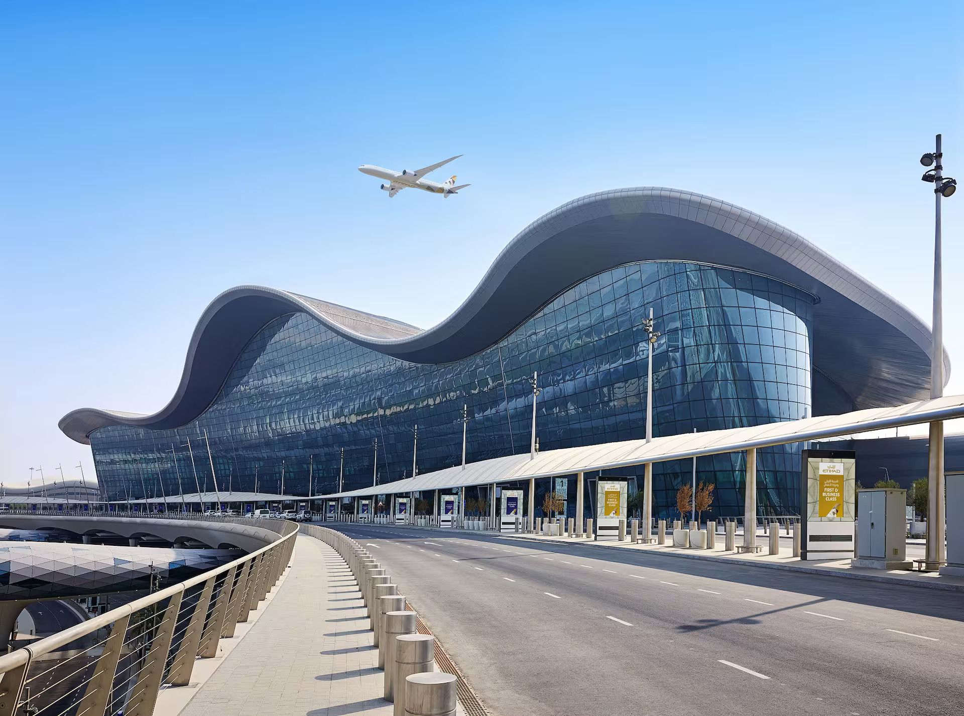 The wave-form roof and curved glass facade of Zayed International Airport in Abu Dhabi, an Etihad aircraft passing overhead.
