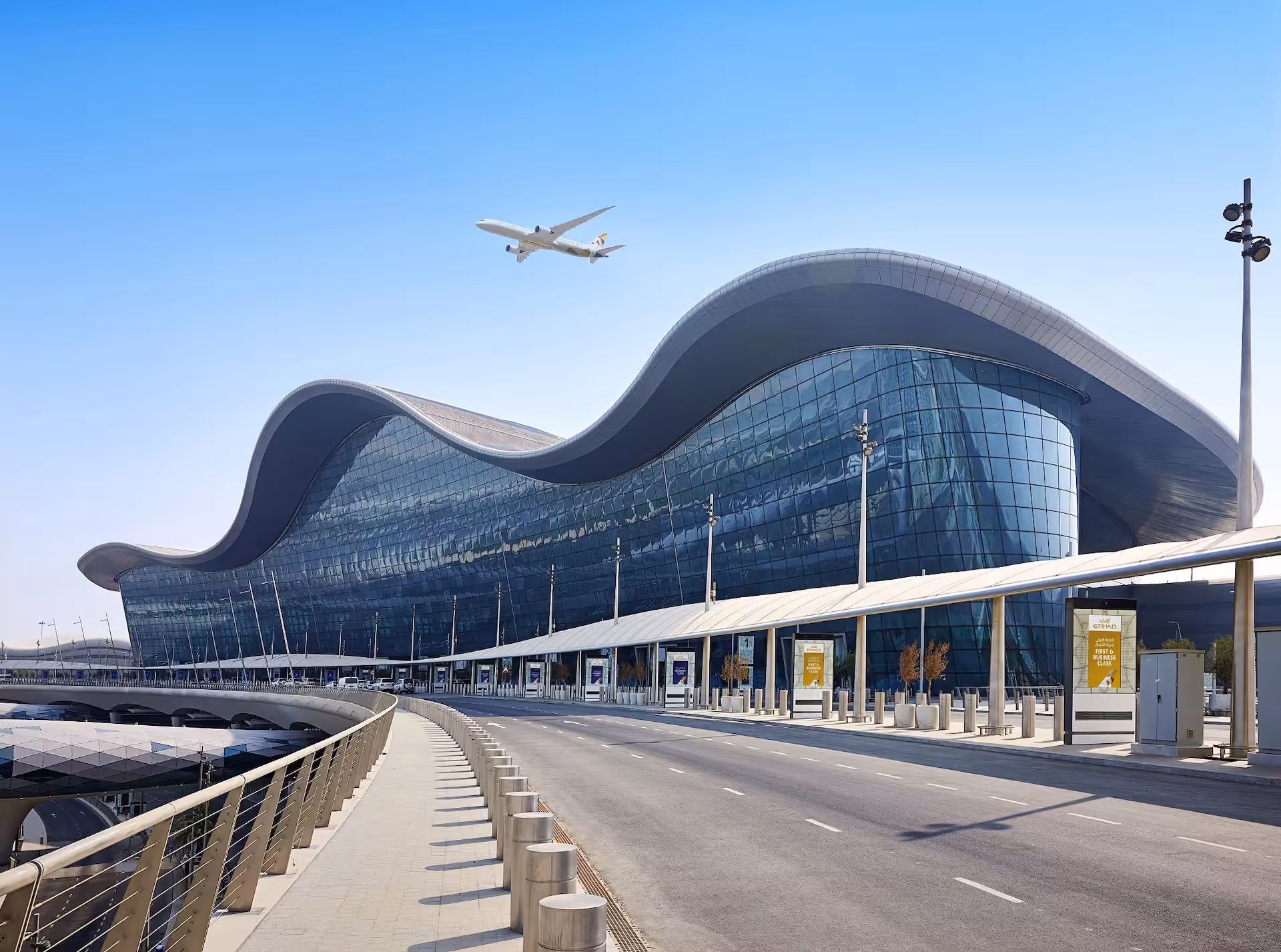 The wave-form roof and curved glass facade of Zayed International Airport in Abu Dhabi, an Etihad aircraft passing overhead.